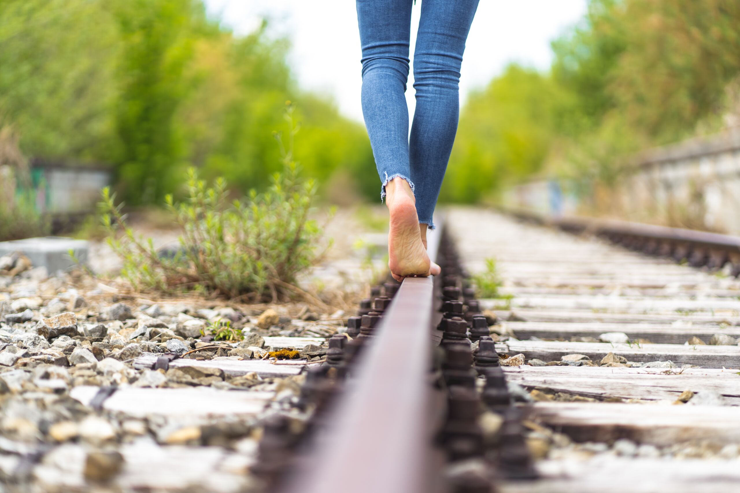 A female in jeans walking through the train rails barefoot